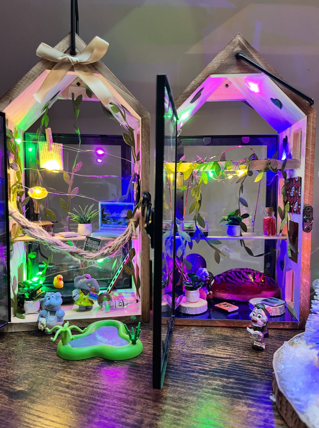 Two miniature glass houses lit up with tiny elephants and plants