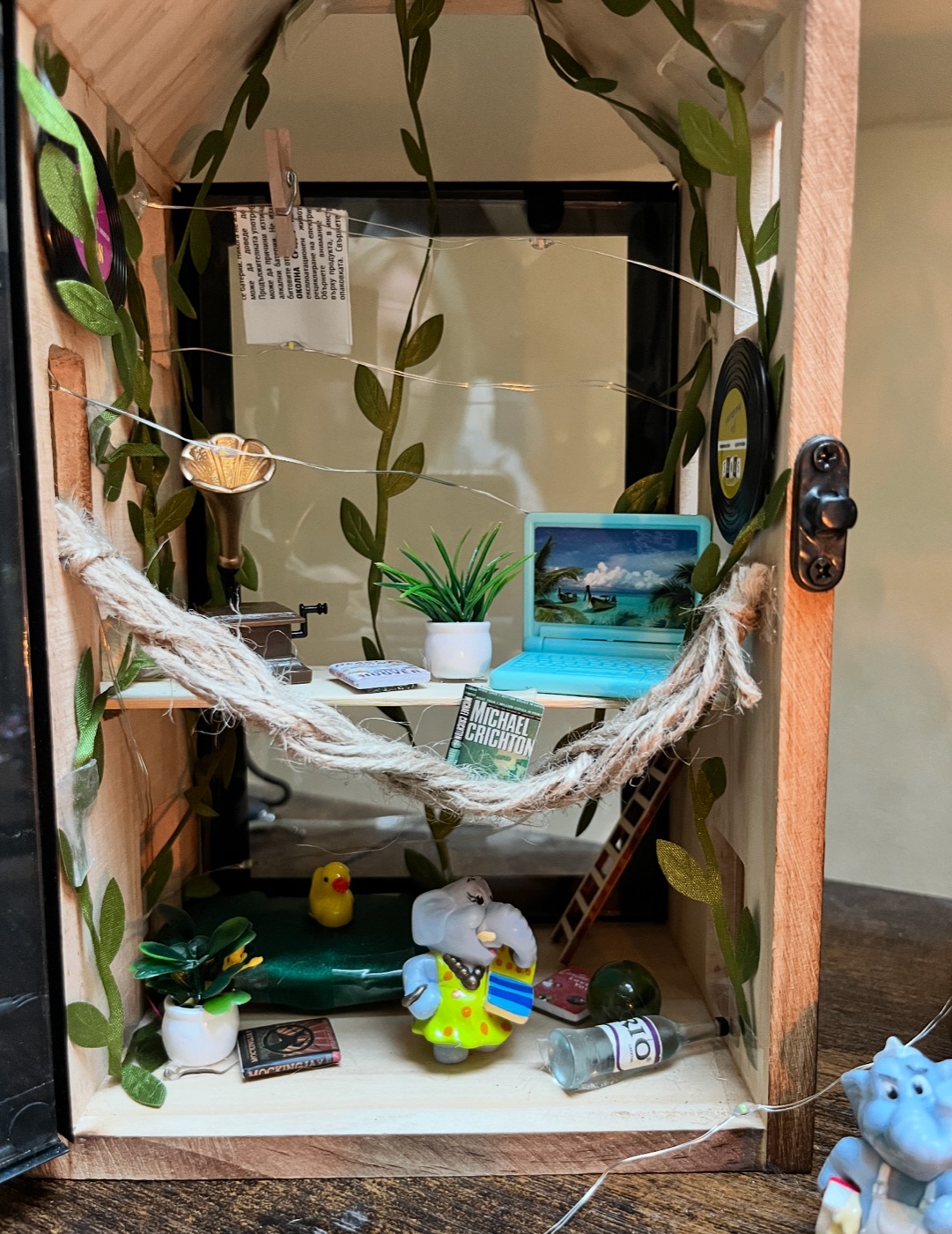 Inside a miniature house — rope hammock, gramophone, books, and vines